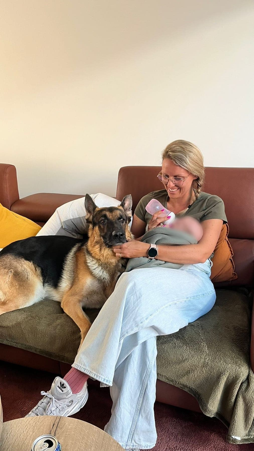 Een Duitse herder ligt rustig naast een mama met haar pasgeboren baby in de zetel