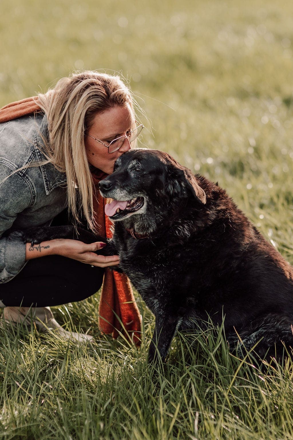 Stéphanie zit gehurkt in het gras en drukt haar neus tegen die van Gust, een oudere zwarte labrador